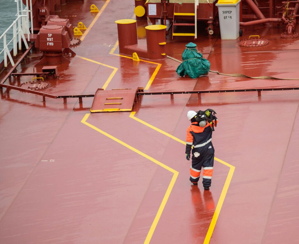 Workers on a cargo ship deck during daytime, wearing protective gear, ensuring safety compliance.