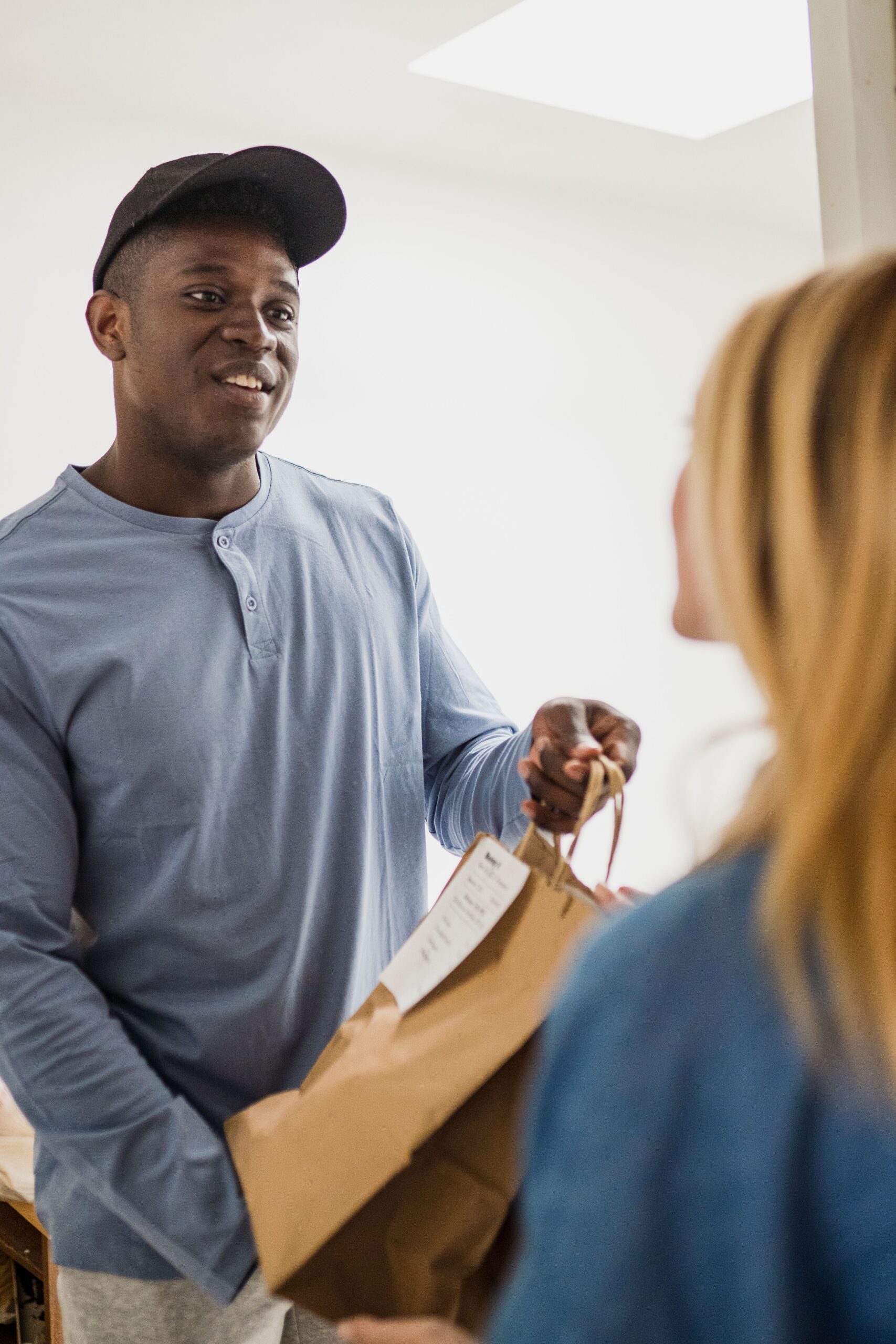 A man delivering a paper bag with a friendly expression indoors, interacting with a customer.