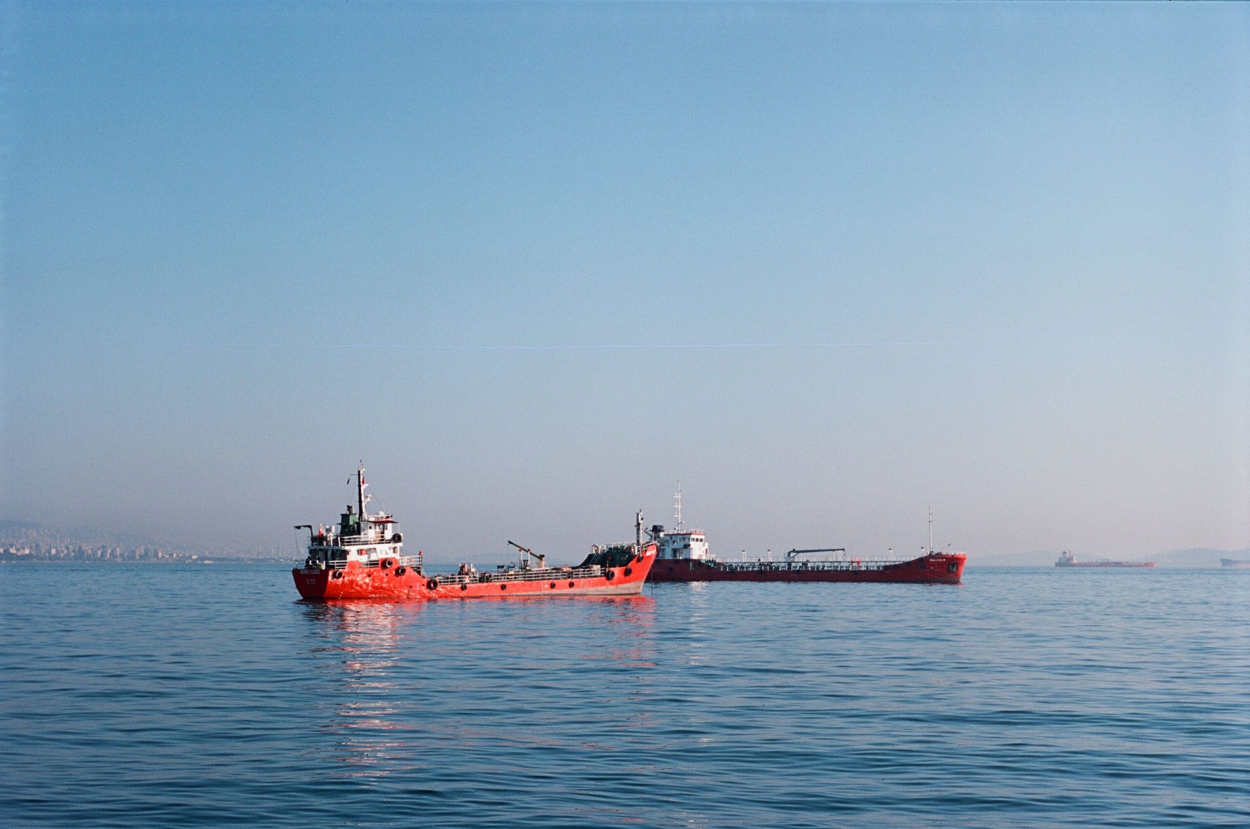 Red cargo ship on tranquil blue sea with distant land visible, ideal for logistics theme.