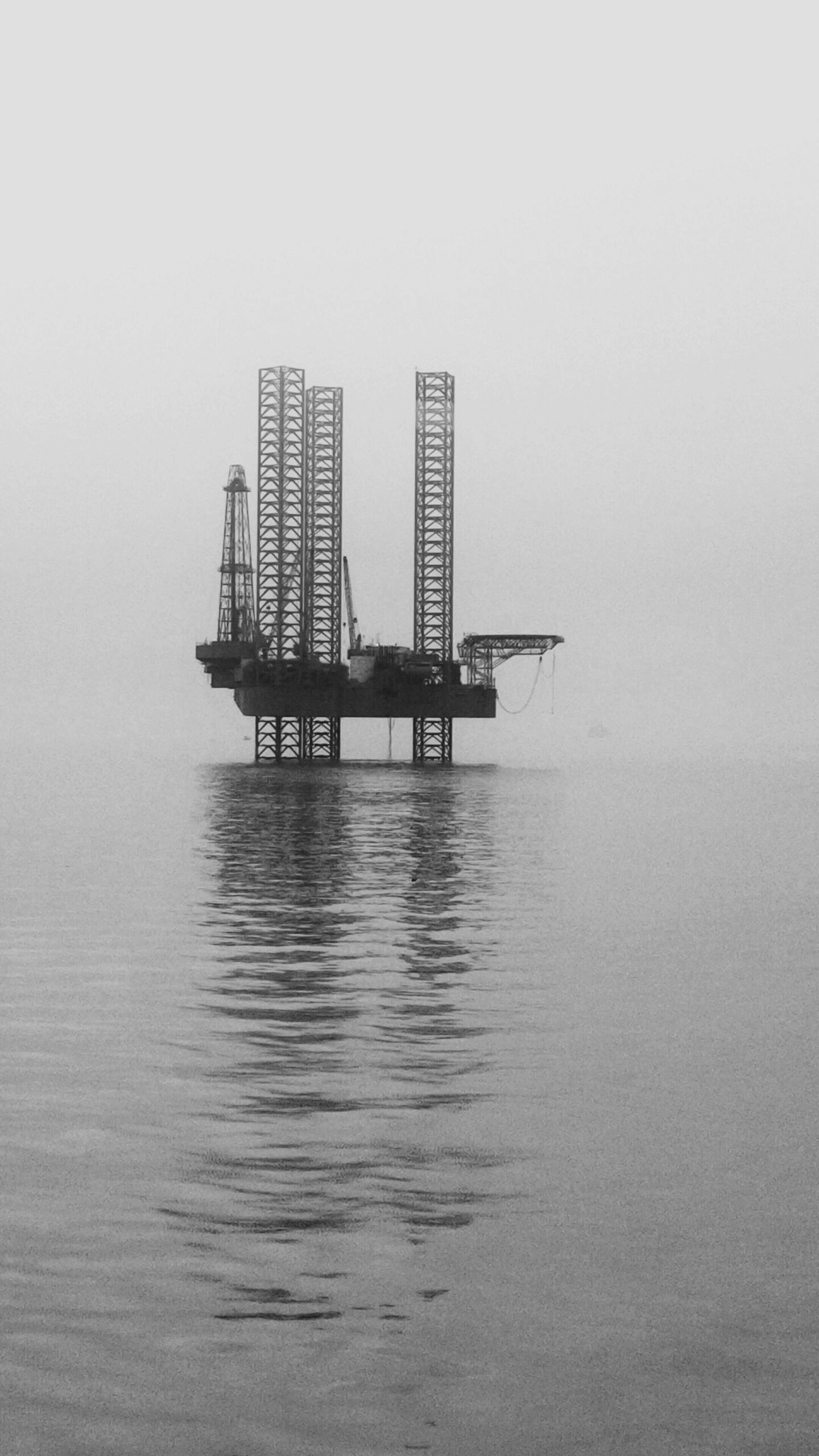 A solitary offshore oil rig stands in a misty sea, captured in a black and white photograph.